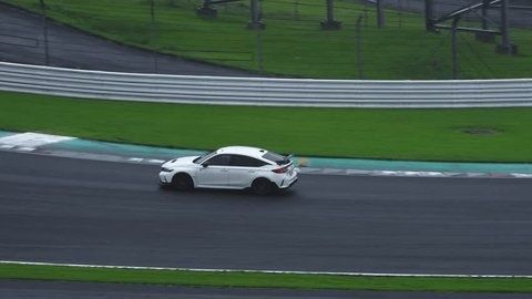 Witte sportwagen rijdt over een nat racecircuit langs de bocht
